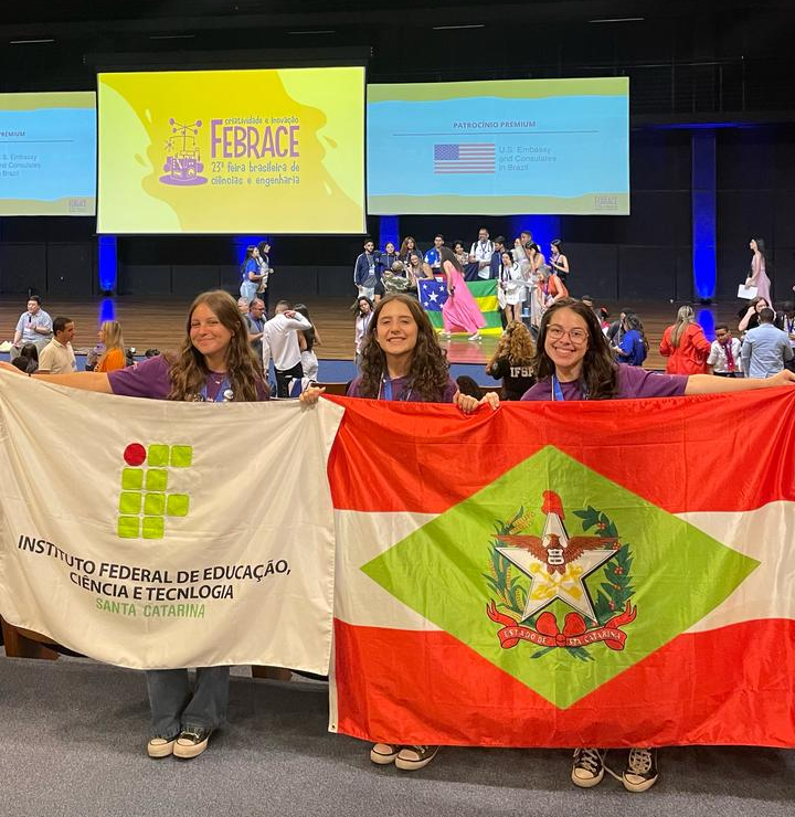 Milena, Karoline e Vitória com as bandeiras do IFSC e de Santa Catarina, durante cerimônia de premiação, em São Paulo